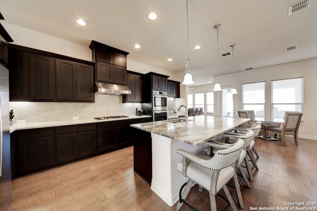 kitchen featuring backsplash, visible vents, under cabinet range hood, and a sink