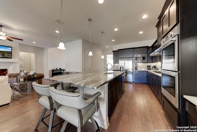 kitchen with a warm lit fireplace, a sink, appliances with stainless steel finishes, a kitchen breakfast bar, and open floor plan