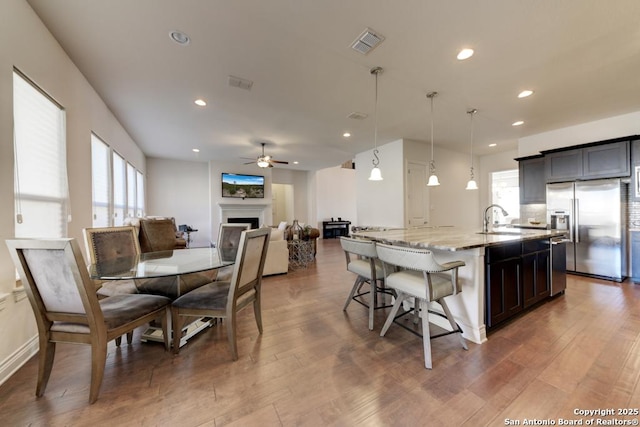 interior space featuring visible vents, a center island with sink, stainless steel refrigerator with ice dispenser, light stone counters, and a fireplace