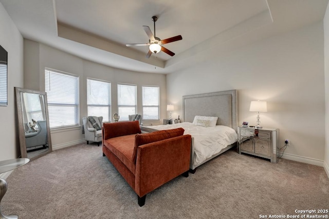 carpeted bedroom with baseboards, a tray ceiling, and a ceiling fan