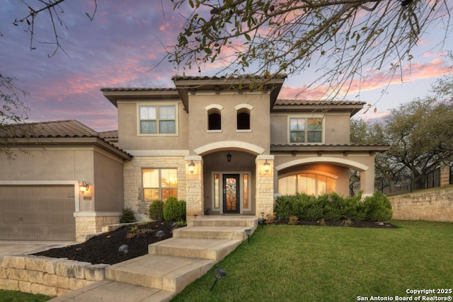 mediterranean / spanish home featuring concrete driveway, a front yard, stucco siding, a garage, and stone siding