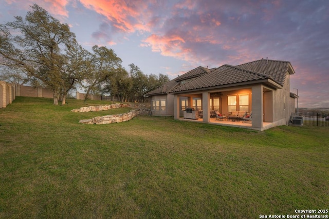 rear view of property featuring a tiled roof, central AC, a yard, a fenced backyard, and a patio area