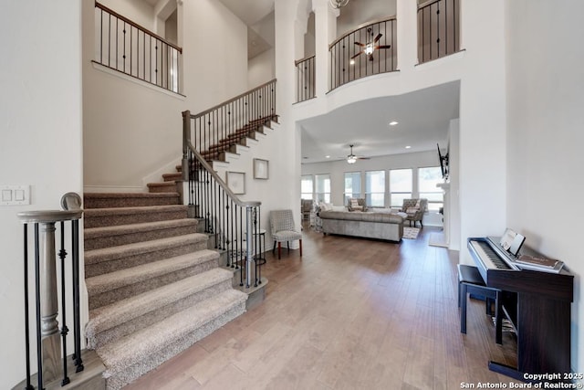 stairway with a towering ceiling, recessed lighting, wood finished floors, and a ceiling fan