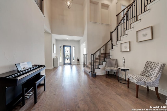 foyer featuring a towering ceiling, stairs, baseboards, and wood finished floors