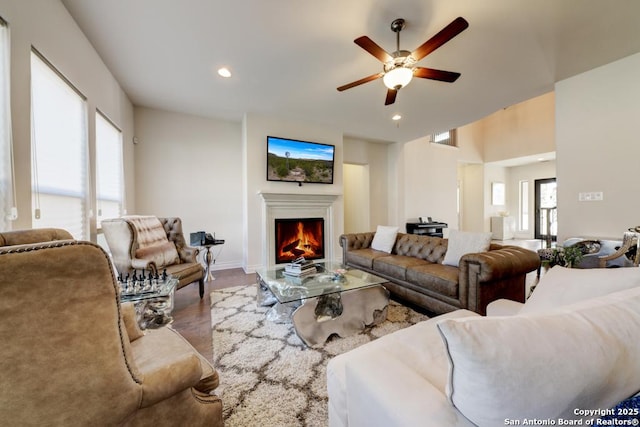 living area featuring a ceiling fan, wood finished floors, baseboards, recessed lighting, and a warm lit fireplace