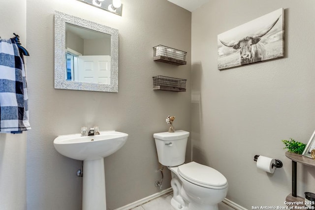 half bath featuring baseboards, toilet, and tile patterned flooring