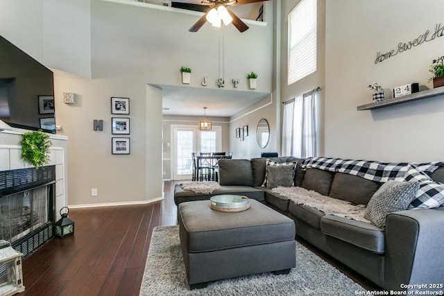 living room featuring dark wood-style floors, baseboards, a high ceiling, ceiling fan, and a tile fireplace