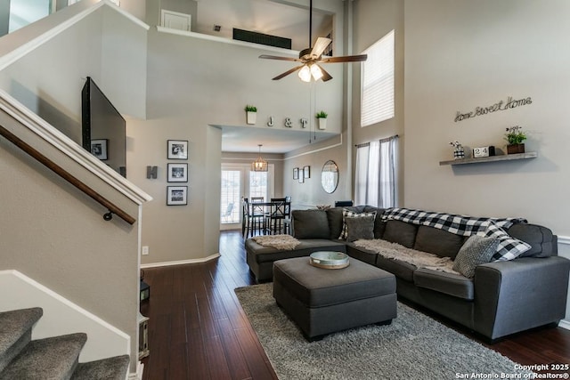 living room featuring ceiling fan, baseboards, stairs, hardwood / wood-style floors, and a towering ceiling