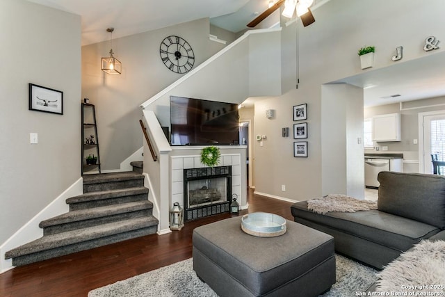 living area featuring stairway, wood finished floors, baseboards, high vaulted ceiling, and a tiled fireplace