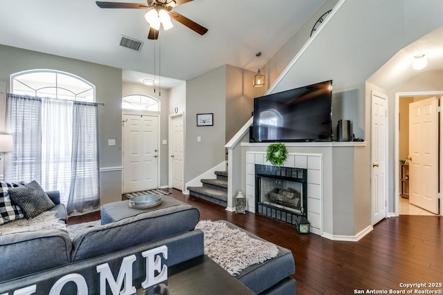 living area featuring visible vents, a tiled fireplace, wood finished floors, ceiling fan, and stairs