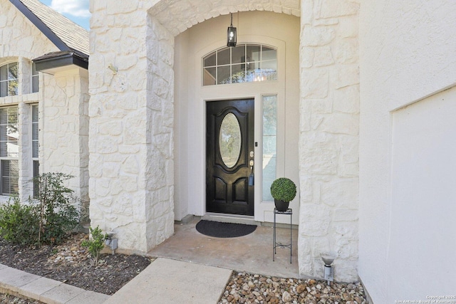 entrance to property with stone siding and a shingled roof