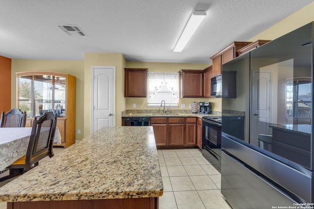 kitchen featuring visible vents, light tile patterned floors, light stone counters, black appliances, and a sink