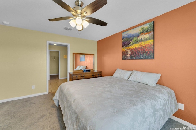 carpeted bedroom with visible vents, baseboards, a walk in closet, and a ceiling fan