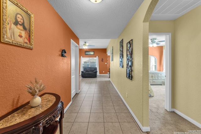 corridor with light tile patterned floors, a textured wall, visible vents, and a textured ceiling