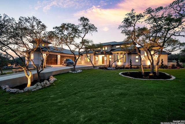 back of house at dusk with a yard, driveway, metal roof, and a standing seam roof