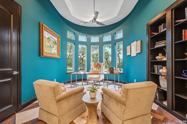 living area featuring a ceiling fan, baseboards, crown molding, a raised ceiling, and a textured wall