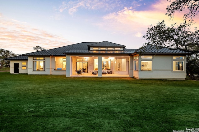 back of property with a standing seam roof, stucco siding, a patio area, a lawn, and metal roof