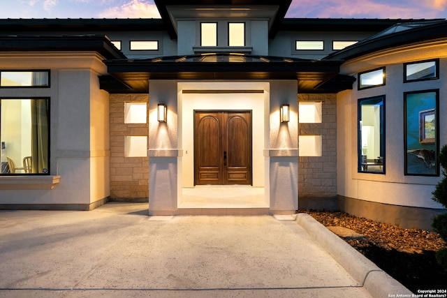 exterior entry at dusk with metal roof, stone siding, and stucco siding