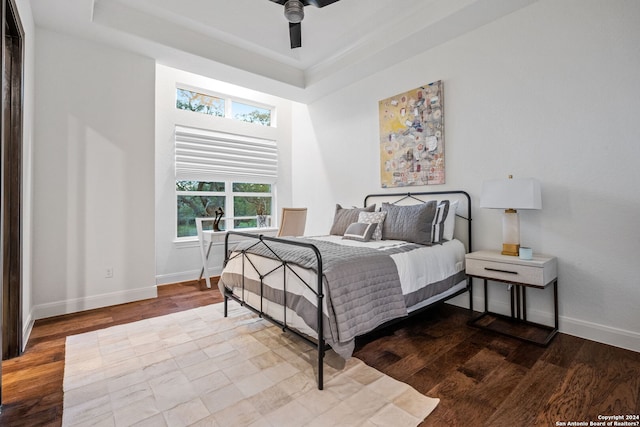 bedroom featuring a ceiling fan, a tray ceiling, baseboards, and wood finished floors