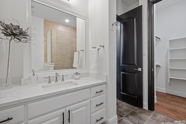 full bathroom with a walk in closet, baseboards, a tile shower, wood finished floors, and vanity