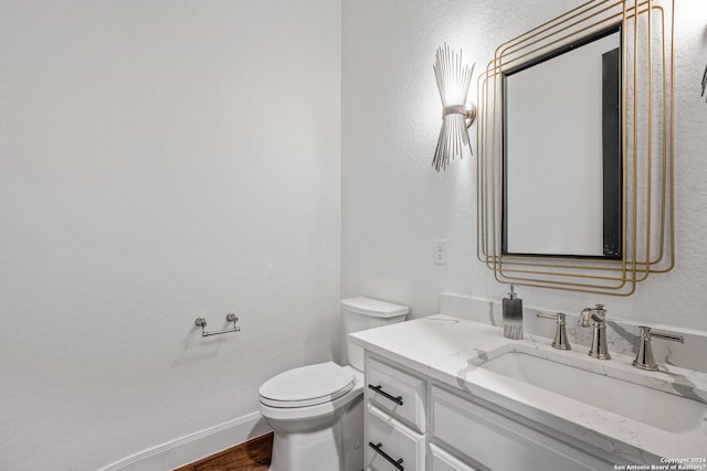 bathroom with vanity, wood finished floors, baseboards, toilet, and a textured wall