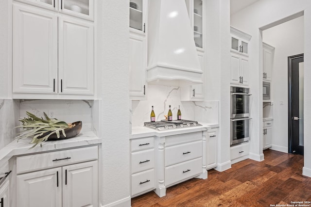 kitchen with dark wood-type flooring, premium range hood, decorative backsplash, appliances with stainless steel finishes, and white cabinetry