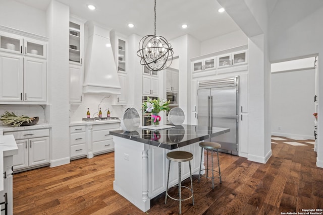 kitchen featuring premium range hood, built in appliances, a kitchen island, and white cabinets