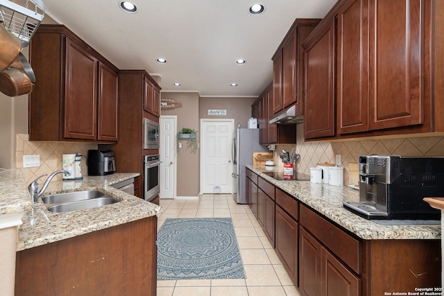 kitchen featuring light stone countertops, under cabinet range hood, appliances with stainless steel finishes, light tile patterned flooring, and a sink