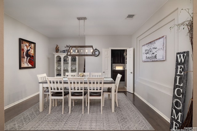 dining room with a notable chandelier, baseboards, visible vents, and dark wood-style flooring