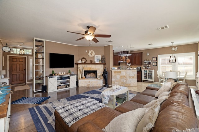 living area featuring light wood-type flooring, visible vents, a ceiling fan, wine cooler, and a stone fireplace