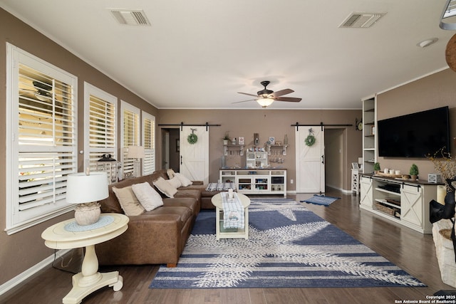 living room with a barn door, wood finished floors, visible vents, and ceiling fan