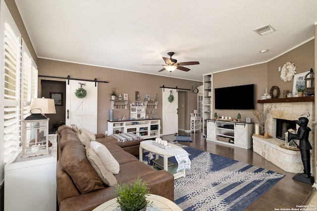 living room with visible vents, ornamental molding, dark wood-style floors, a barn door, and ceiling fan