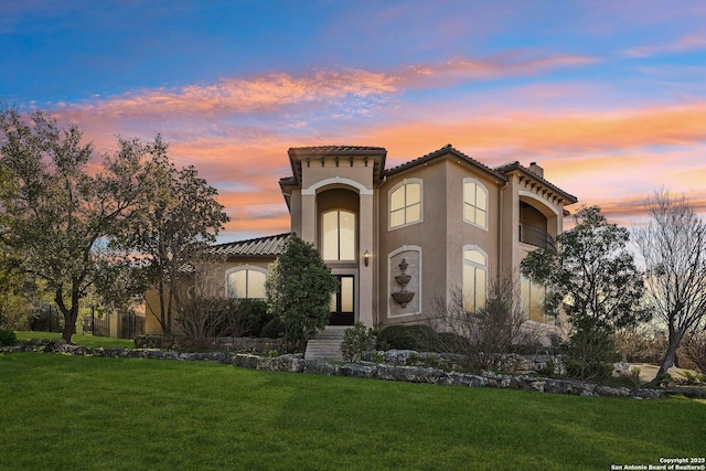 mediterranean / spanish house with a front lawn, a tiled roof, a chimney, and stucco siding