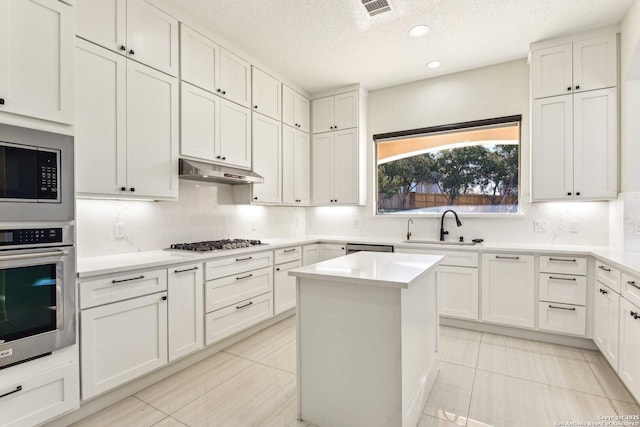 kitchen with under cabinet range hood, a sink, stainless steel appliances, light countertops, and decorative backsplash