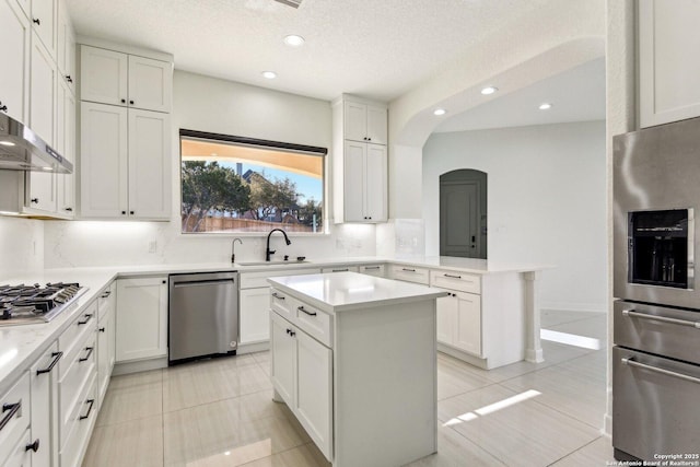 kitchen with a peninsula, arched walkways, a sink, decorative backsplash, and appliances with stainless steel finishes