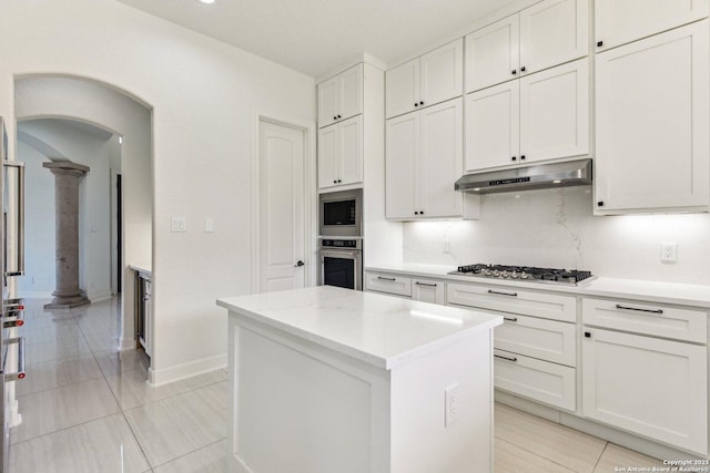 kitchen with under cabinet range hood, a kitchen island, white cabinetry, stainless steel appliances, and arched walkways