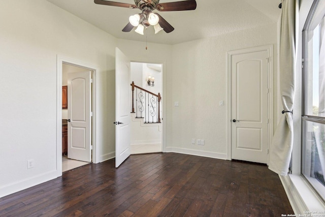 spare room with a ceiling fan, baseboards, dark wood-type flooring, and stairs