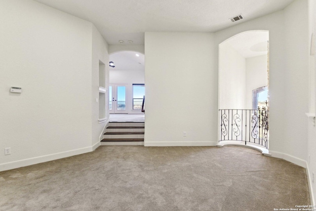 carpeted empty room featuring arched walkways, visible vents, and baseboards