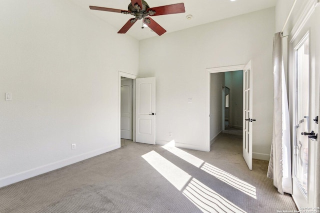 unfurnished bedroom with light carpet, multiple windows, a high ceiling, and baseboards