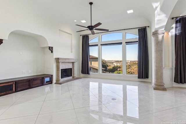 unfurnished living room with a ceiling fan, arched walkways, ornate columns, and a premium fireplace