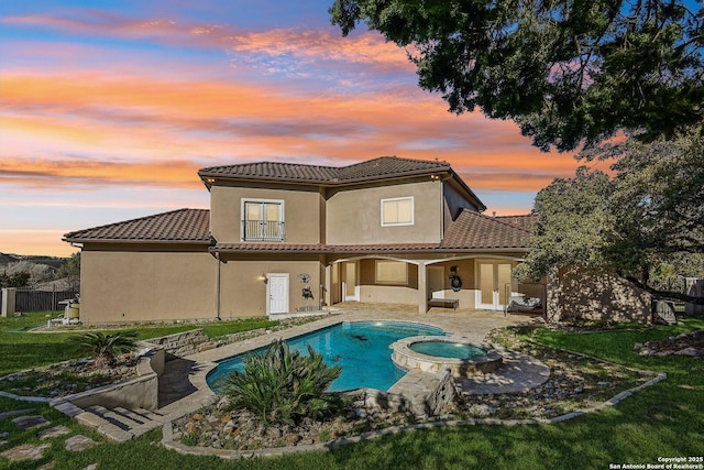 back of property featuring stucco siding, a pool with connected hot tub, a tile roof, a patio, and a yard