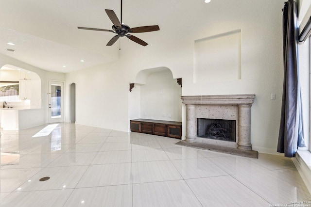 unfurnished living room with light tile patterned floors, arched walkways, ceiling fan, and a fireplace