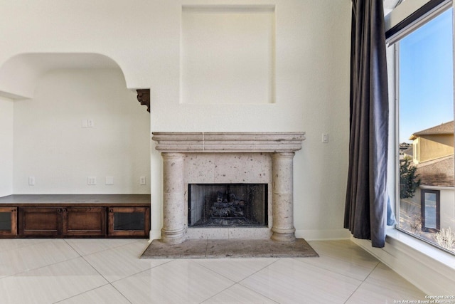 unfurnished living room with light tile patterned floors, baseboards, arched walkways, and a fireplace