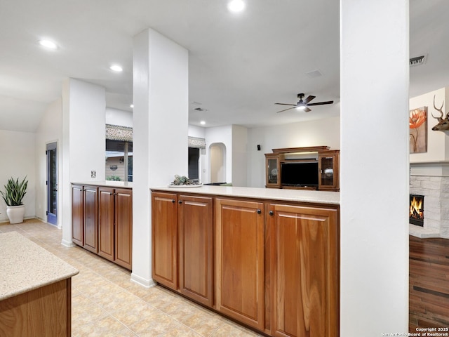 kitchen featuring brown cabinetry, visible vents, a fireplace, light countertops, and open floor plan