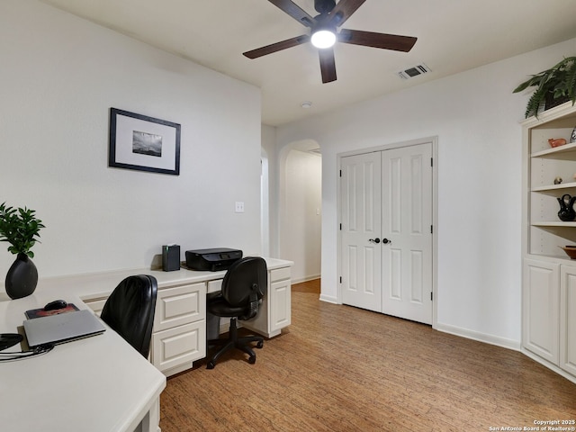 home office with visible vents, a ceiling fan, arched walkways, light wood-style floors, and baseboards