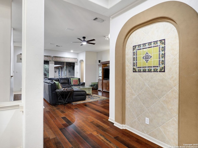 hallway featuring dark wood-style floors, visible vents, arched walkways, and baseboards