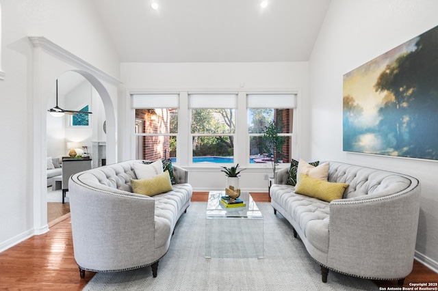 living area with arched walkways, a healthy amount of sunlight, lofted ceiling, and wood finished floors