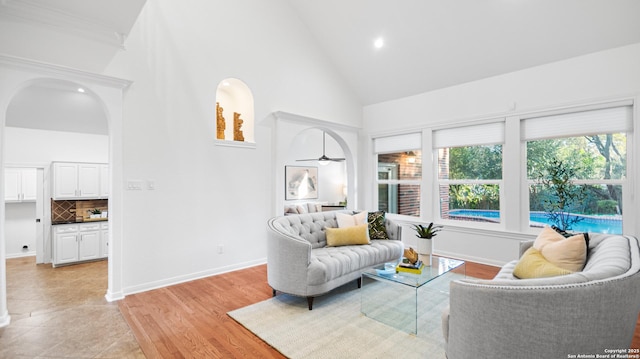 living room featuring light wood-type flooring, baseboards, arched walkways, and high vaulted ceiling