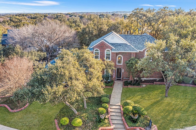 view of front of home with a front lawn, a view of trees, brick siding, and a shingled roof