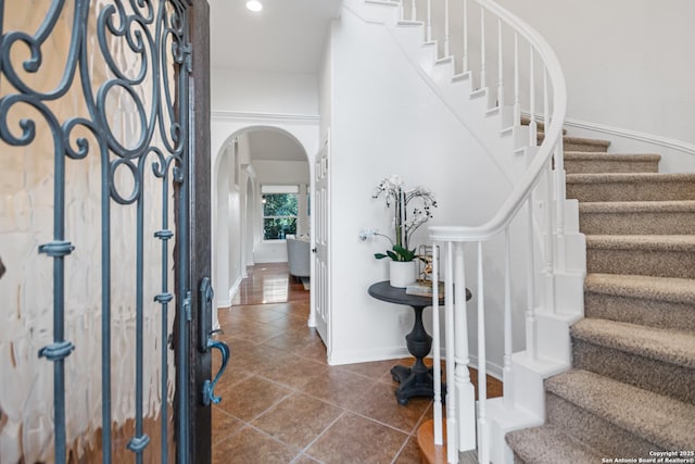 entryway with stairway, baseboards, dark tile patterned flooring, recessed lighting, and arched walkways